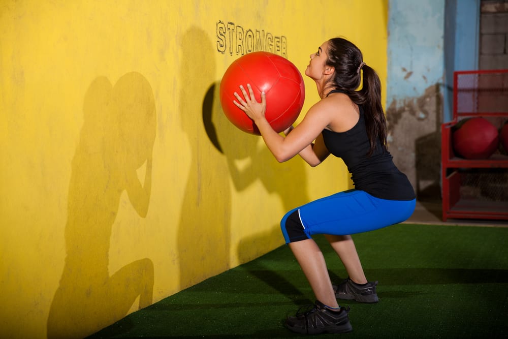 young woman does squat plus wall throw with medicine ball